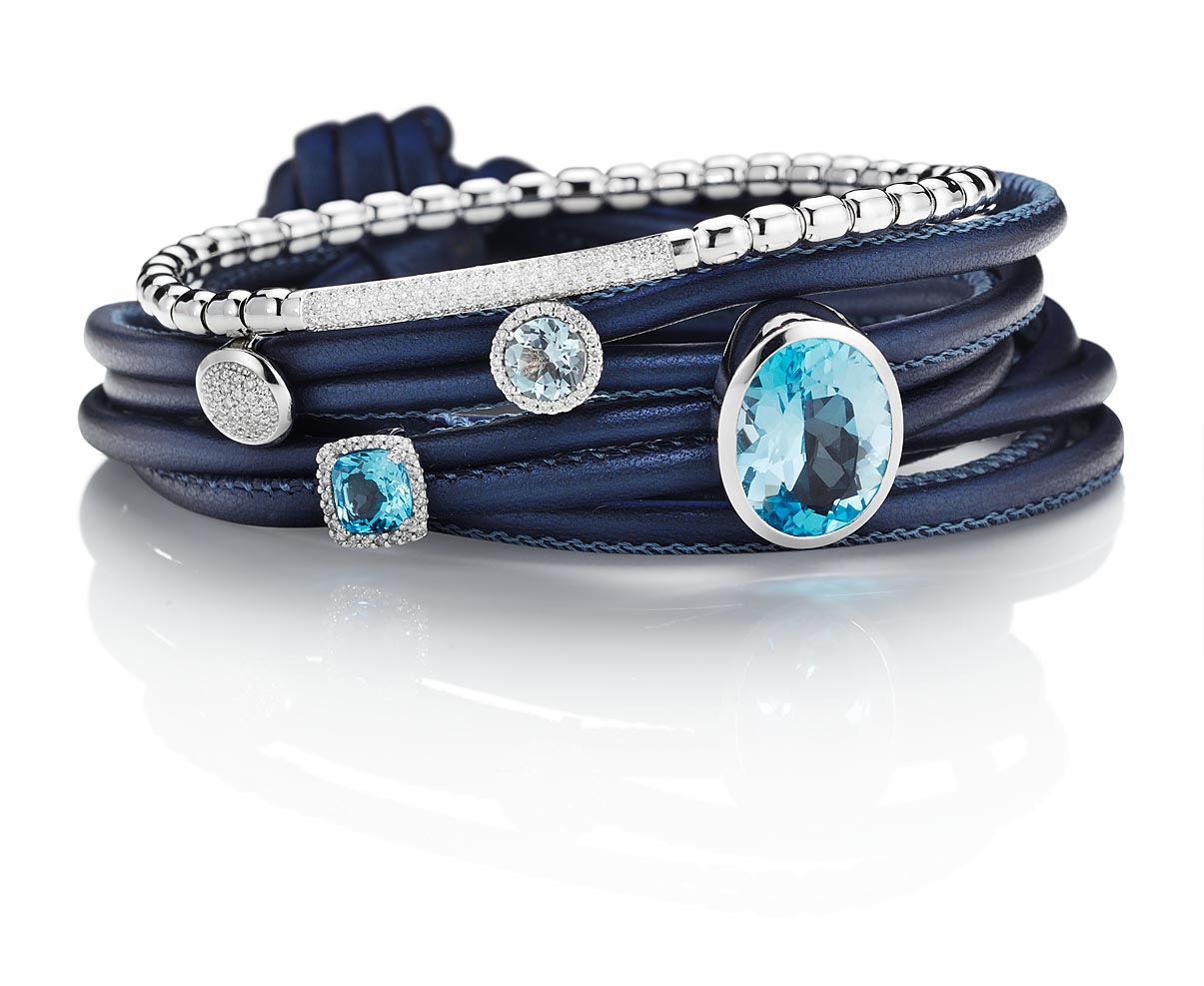 Werbeaufnahme von einem Lederband blau mit Farbsteinen und Diamanten auf spiegelndem Untergrund