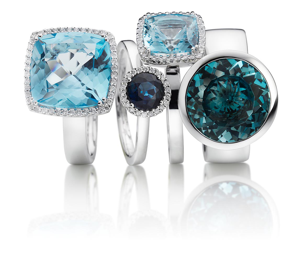 Sachaufnahme im Studio von vier Ringen silber mit blauen Farbsteinen auf weißem Untergrund